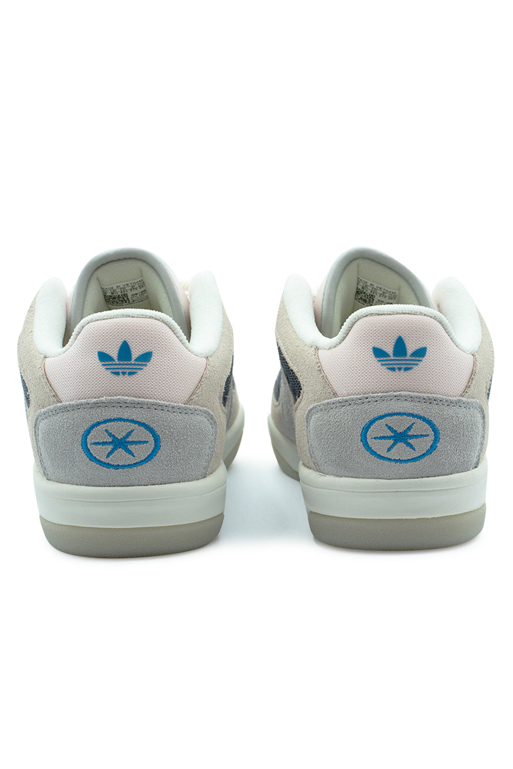 Rear perspective shot of the heels of the Adidas Bad Bo 1.1 sneakers, displaying the pastel pink textile heel tabs embroidered with cyan blue Trefoil logos, layered over grey suede heel counters featuring Bad Bunny's signature blue third-eye oval logo, grounded by an off-white rubber midsole