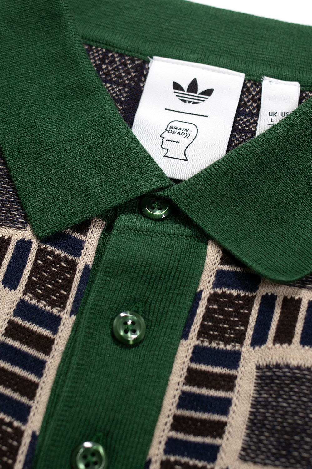 Detailansicht des Adidas x Brain Dead Poloshirts mit Trefoil Logo und charakteristischer Knopfleiste in Kontrastfarbe.