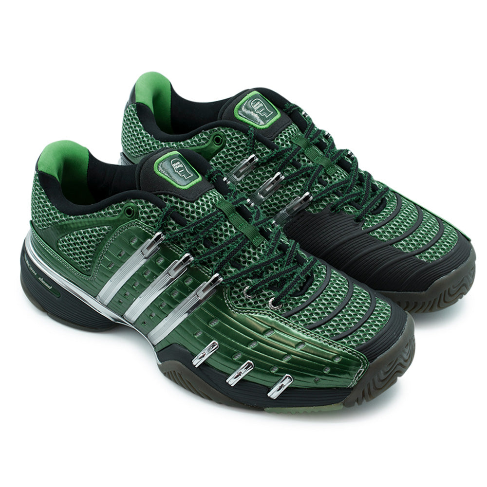 Three-quarter studio perspective of the adidas x Brain Dead Barricade V sneakers, highlighting the heavy-duty court chassis, shiny chrome midfoot eyelet anchors, ribbed protective forefoot panels, two-tone laces, and molded green tongue badges.