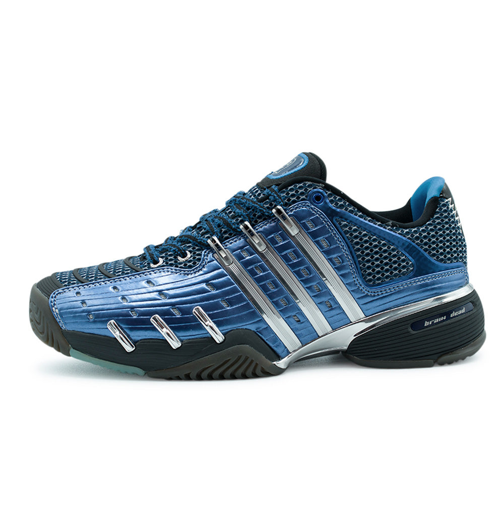 Lateral profile studio view of the adidas x Brain Dead Barricade V shoe in Mystery Ink, Silver Metallic, and Carbon, showcasing the glossy metallic royal blue ribbed synthetic overlays, open-cell mesh base, polished mirror-chrome Three Stripes support cage, sculpted carbon black midsole, and lateral heel "brain dead" branding badge.