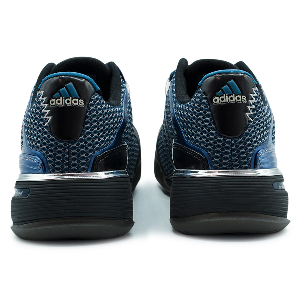 Rear studio view of the adidas x Brain Dead Barricade V heels, displaying the layered open-hole mesh collars, glossy patent leather heel counters, bright blue embroidered adidas Performance triangle logos, mirror-finish silver metallic midsole shanks, and embossed branding across the textured carbon outsoles.