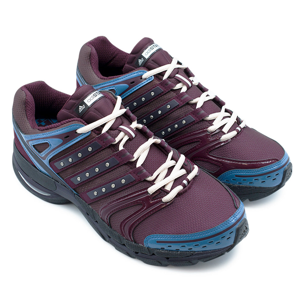 Angled three-quarter perspective of the Adidas X Hardies Adistar Control 5 running shoes, highlighting the Y2K performance runner silhouette, patent leather mudguards, embedded crystal accents across the side stripes, and durable black rubber outsoles.