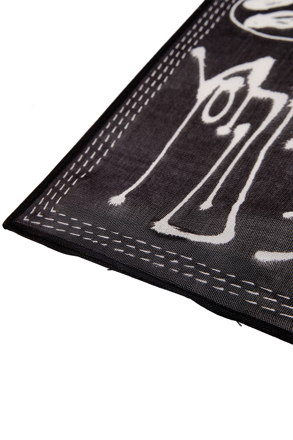 Close-up angle shot of the corner of the black Adidas Y-3 X Chito silk-cotton bandana, showcasing the fine woven fabric texture, rolled hem with triple white dash-line stitching, and a white airbrushed Yohji dripping graffiti signature tag.