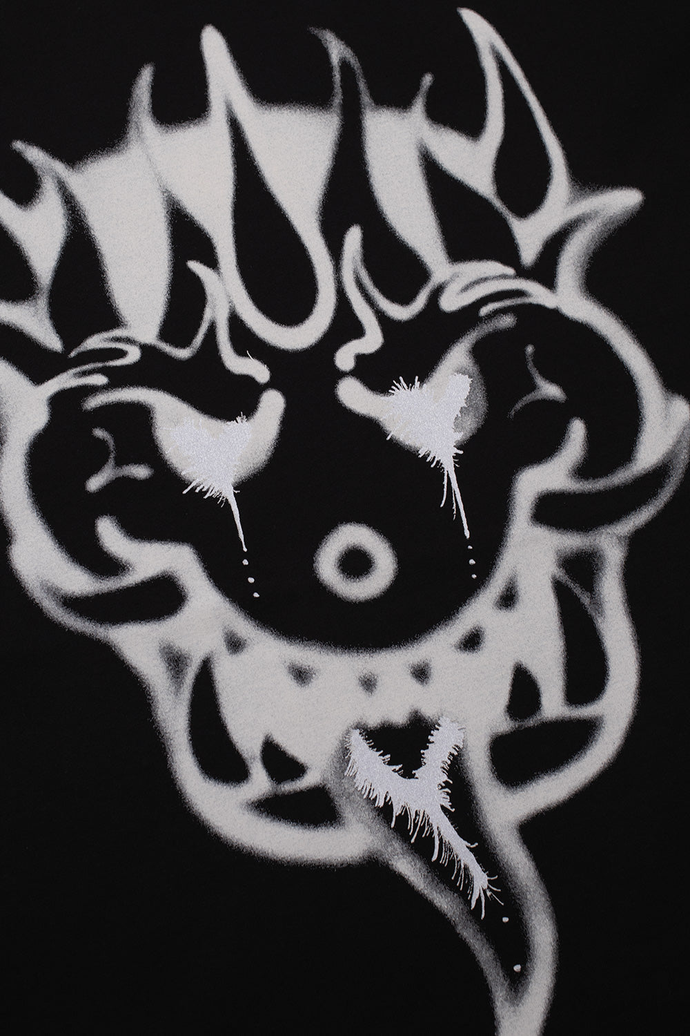 Detailed close-up shot of the white airbrushed monster face artwork printed on the black cotton jersey chest of the Adidas Y-3 X Chito GFX tee, highlighting glowing stencil eyes, fine spray splatters, and dripping paint details.