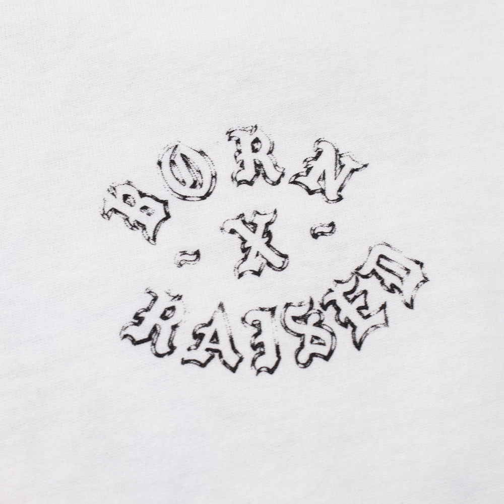 Macro studio close-up of the front chest graphic on the white Born X Raised Fantasy Rocker T-Shirt, detailing the black-and-grey screen-printed ink forming the circular arched "BORN X RAISED" rock-and-roll typography with fine stippled shading on textured cotton fabric.