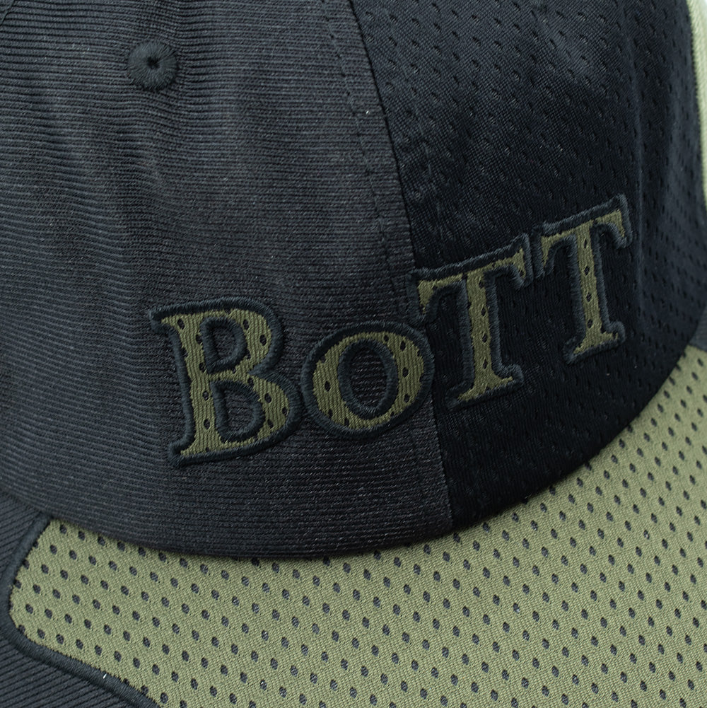 Detailed macro studio close-up of the front crown on the BoTT Mesh Paneled Cap Olive, highlighting the perforated mesh fabric texture, embroidered eyelet, curved visor insert seam, and the olive green thread embroidery forming the bold serif "BOTT" lettering with black outline detailing.