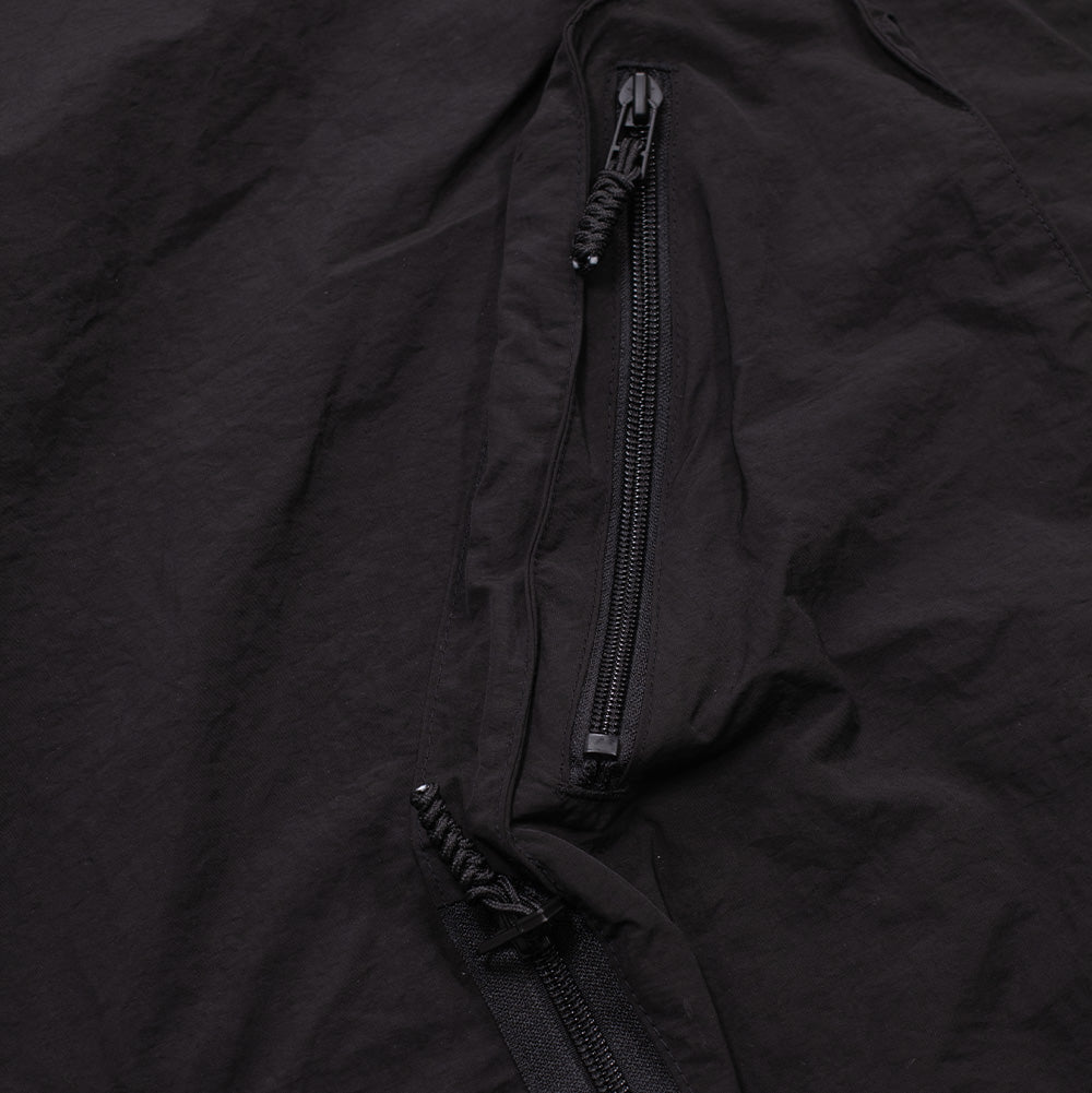 Macro view of the utility cargo pocket construction on the Brain Dead Dolman Sleeve Jacket, detailing the deep pleating of the 3D pocket volume and the vertical reverse-coil zipper with a braided textured pull loop set against the crisp matte shell material.