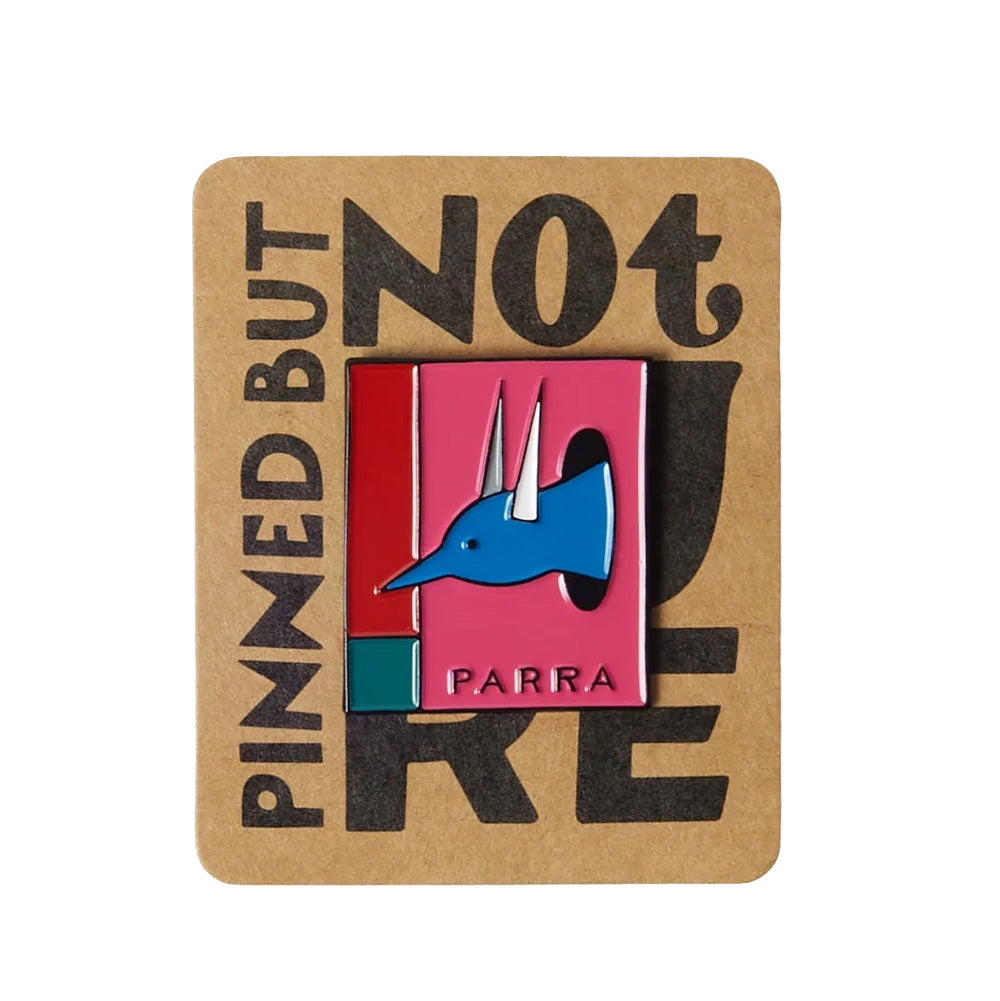 Studio top-down flat lay view of the By Parra The Hunted Enamel Pin in Pink, mounted on its original brown cardboard backing card reading "PINNED BUT NOT LIKE", featuring a rectangular glossy hard enamel metal pin measuring 3.3 cm by 3 cm with polished silver-tone metal borders, color-blocked panels in red, teal green, and vibrant pink, and an illustrated blue bird-hybrid creature emerging from a black portal above debossed "PARRA" branding.