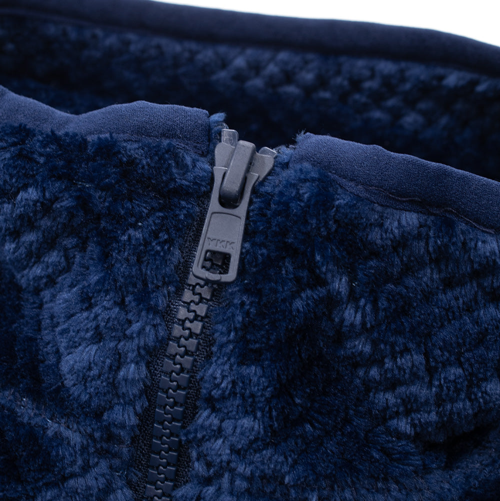 Macro studio close-up of the neckline on the Dancer Fleece Half Zip, highlighting the matte navy YKK zipper puller and chunky teeth set into deep textured sherpa fleece, finished with elastic piping along the upper collar rim.