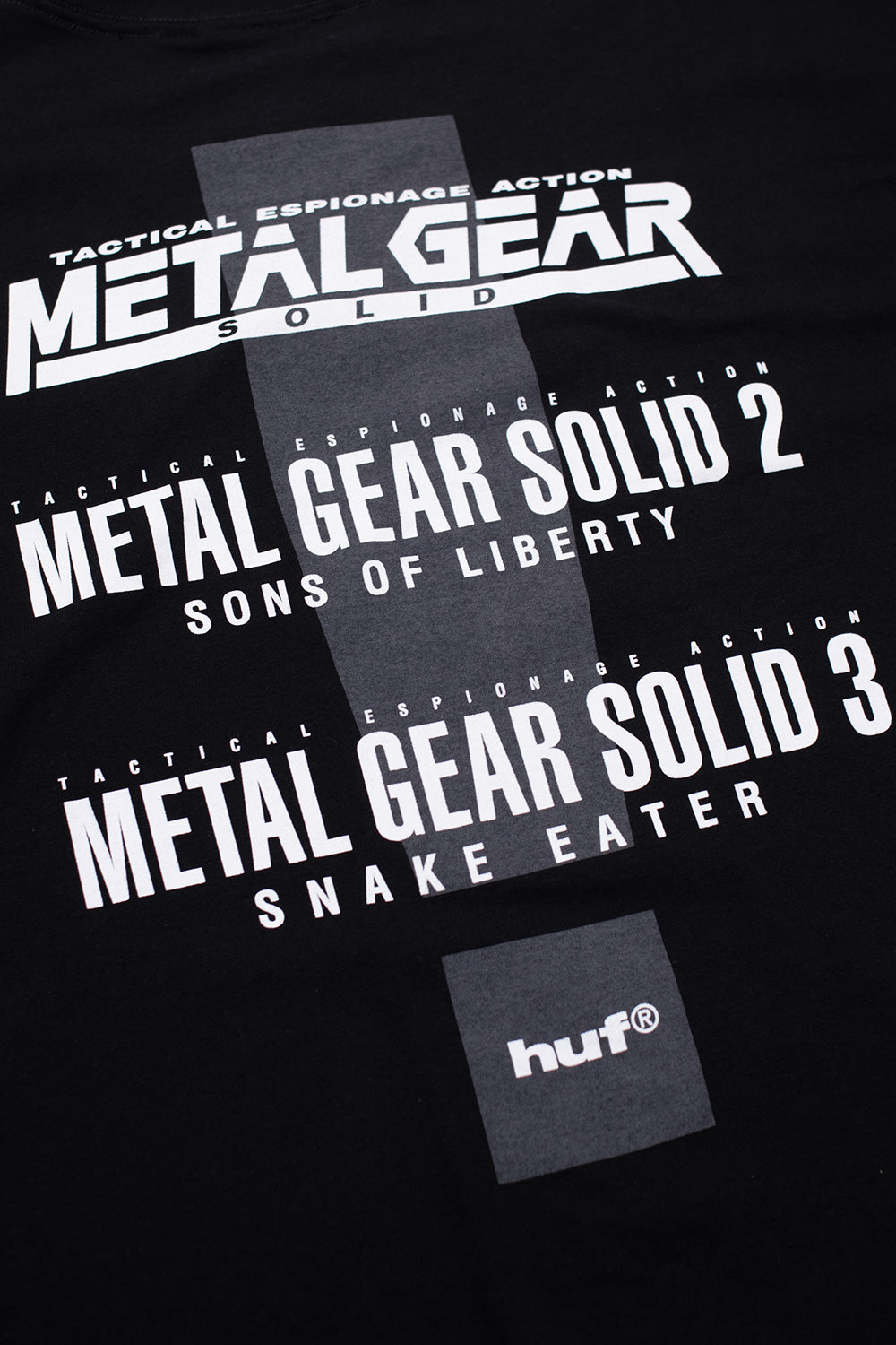 Detail shot of rear typography print on HUF x Metal Gear Solid black T-shirt displaying tactical espionage action branding and official franchise titles