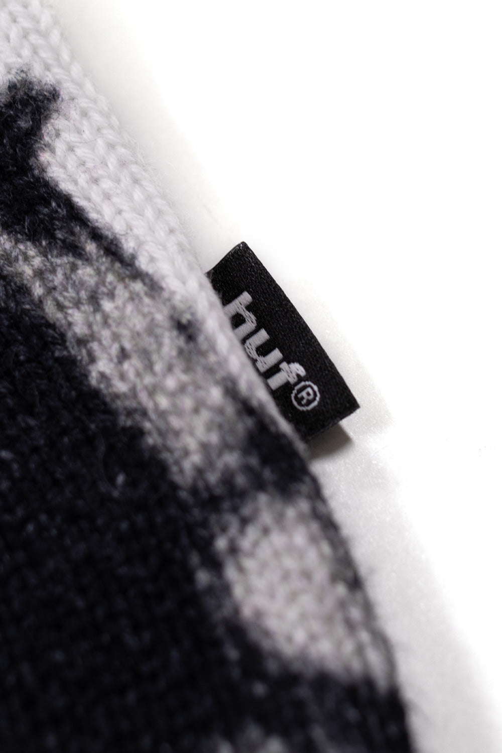Detail shot of HUF woven label on Metal Gear Solid MGS2 white crewneck sweater with ribbed cuffs and all-over graphic print