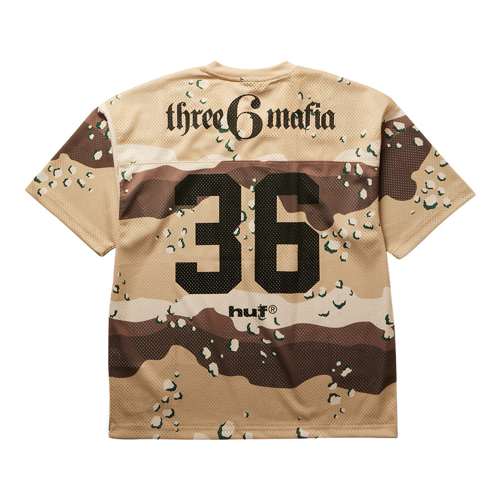 Back flat lay view of the Huf X Three 6 Mafia Football Jersey in desert camo mesh, showcasing stylized gothic "three 6 mafia" lettering across the upper shoulders, an oversized black athletic jersey block number "36" printed across the back panel, and a black "huf®" logo printed at the lower hemline.