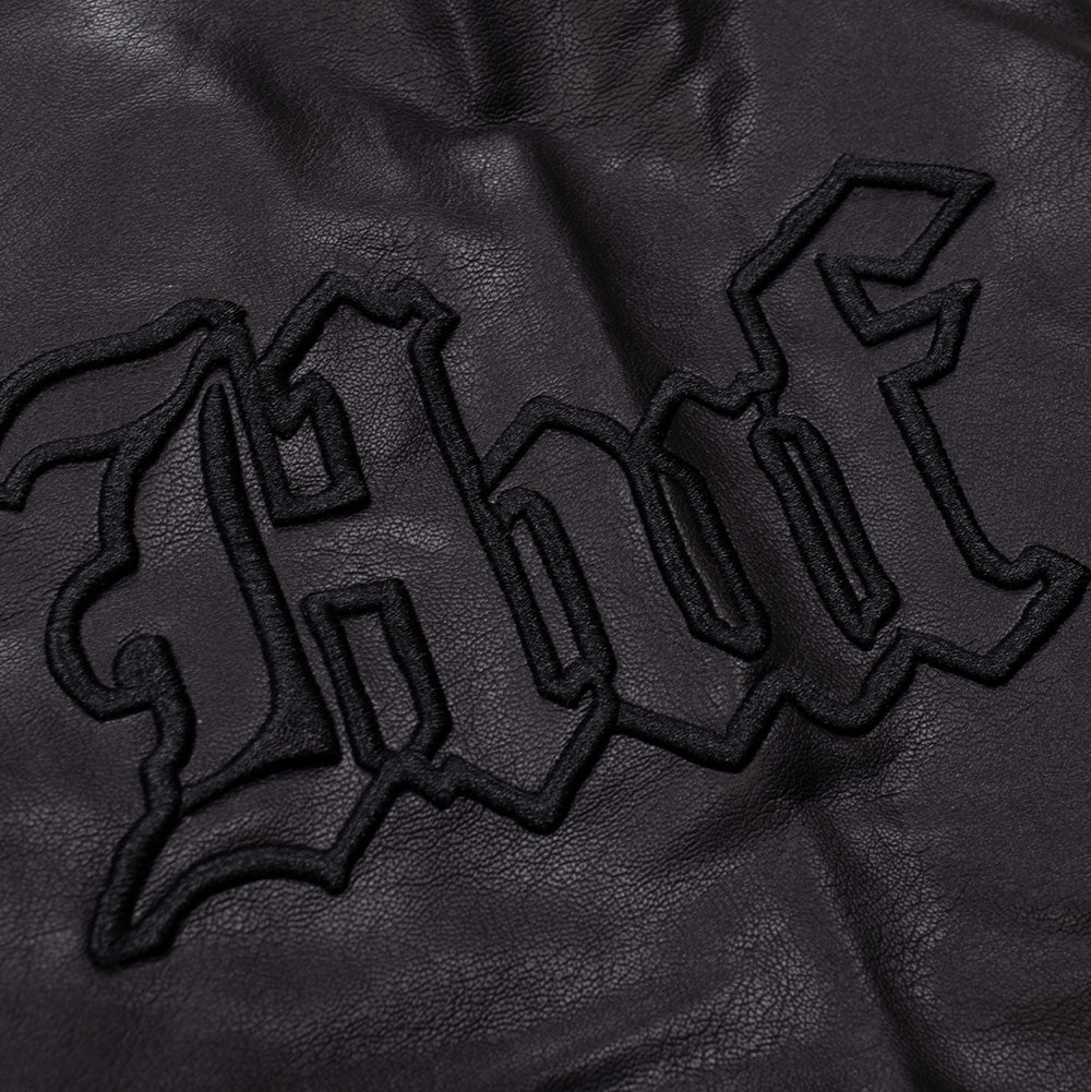 Macro close-up perspective of the sleeve on the Huf X Three 6 Mafia jacket, highlighting the prominent tonal black embroidered Old English Gothic "HUF" lettering with heavy satin-stitch borders.