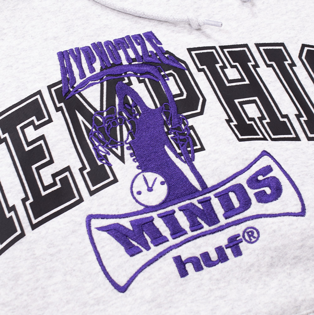 Macro studio close-up of the chest embroidery on the Huf X Three 6 Mafia Memphis Hoodie, highlighting the detailed purple satin-stitched reaper emblem with clock and hourglass, arched "HYPNOTIZE" and "MINDS" script, layered over the black tackle-twill "MEMPHIS" lettering with white borders.