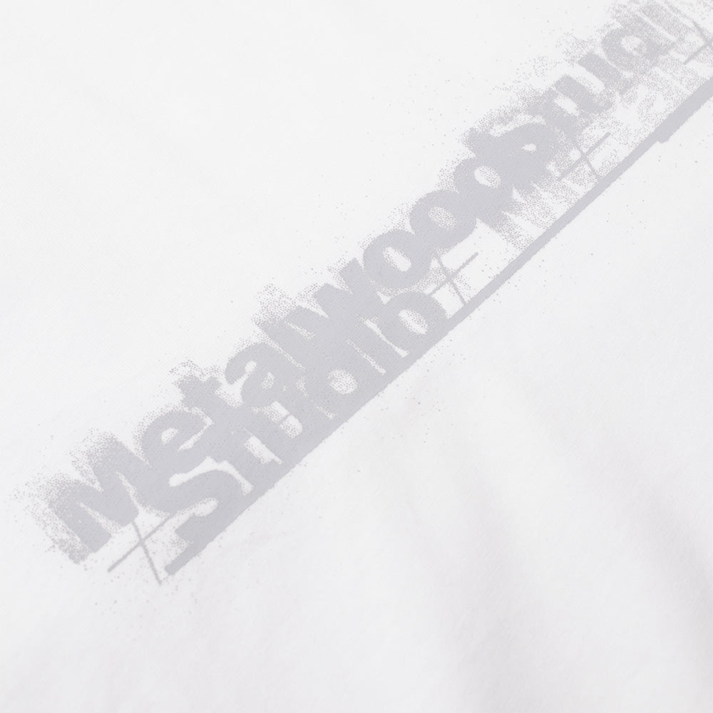 Detailed macro perspective of the chest print on the white Metalwood Studio Skidmark T-Shirt, capturing the stippled halftones and airbrushed gradient overspray effect defining the silver-grey "Metalwood Studio" typeface framed by subtle linear grid accents across the white cotton knit fabric.