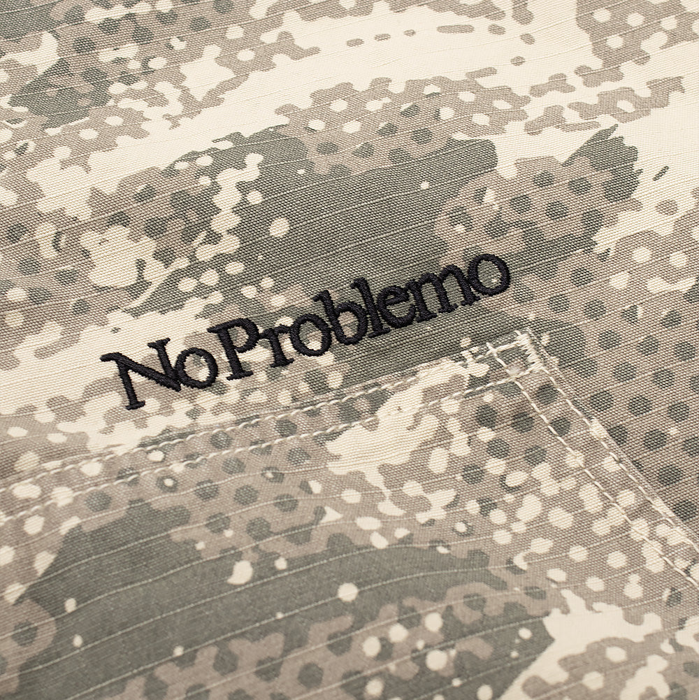 Detailed macro perspective of the pocket embroidery on the Aries No Problemo Forest Ripstop Work Jacket, displaying the dense black satin-stitch thread spelling out "No Problemo" in serif typography set cleanly against the sand, grey, and khaki dot-matrix camouflage pattern on durable ripstop canvas.