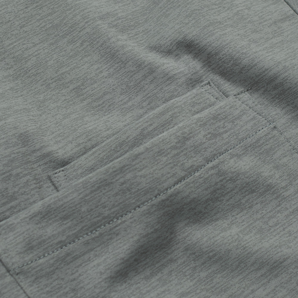 Detailed macro perspective of the top pocket hem on the Acrid Green Oakley FGL Scratch Tee, highlighting the reinforced bartack corner stitching, clean topstitching, and the fine-gauge heathered green technical fabric weave.