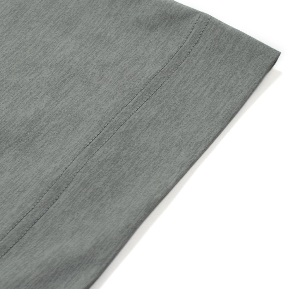 Macro studio perspective of the bottom hem and side edge on the Oakley FGL Scratch SS Tee in Acrid Green, showing the clean parallel double-needle stretch hem stitching and the finely textured melange surface of the technical moisture-wicking material.