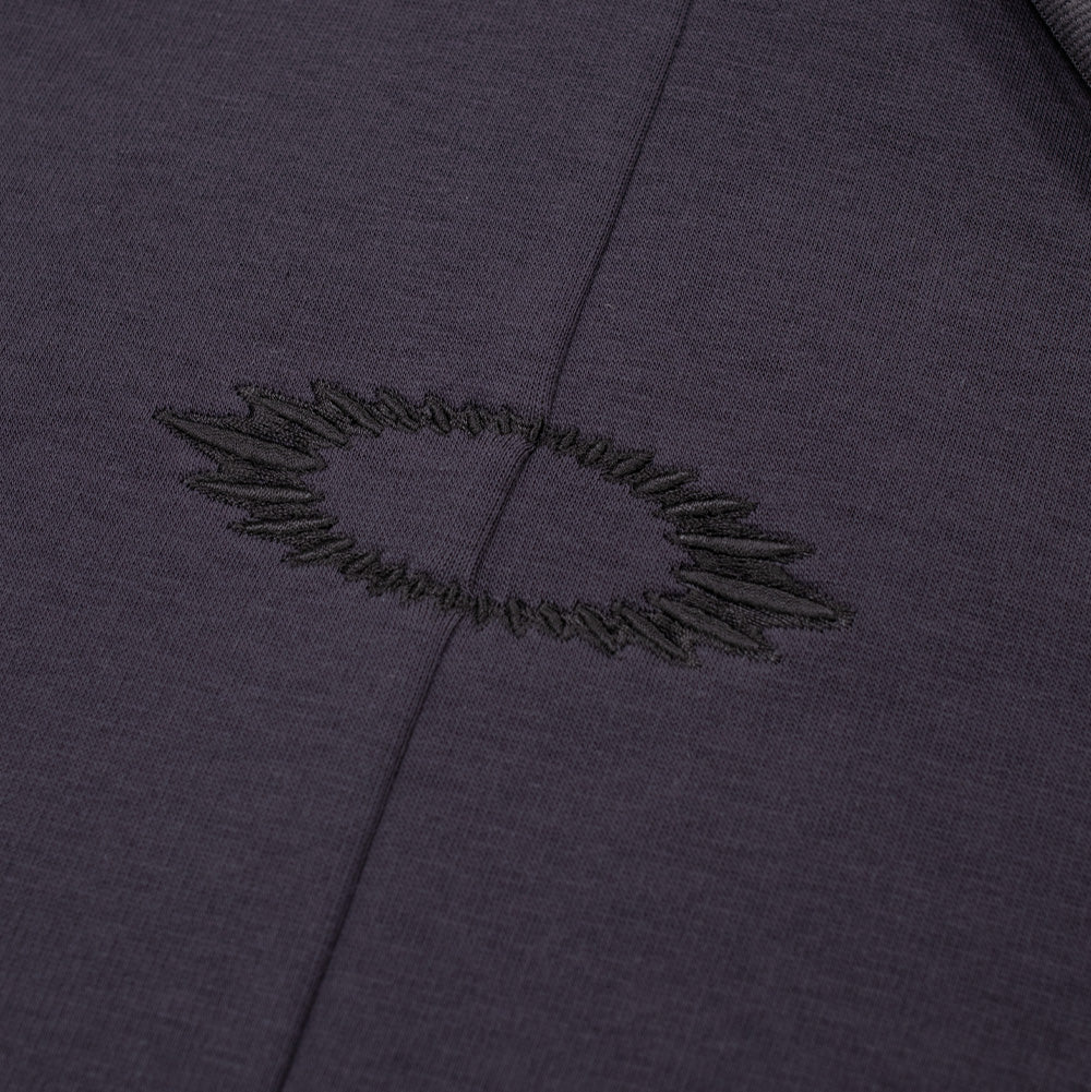 Macro view of the center chest embroidery on the Phantom Oakley FGL Slick Fleece Hoodie, highlighting the tonal black satin-stitch thread forming a radiated, soundwave-style scratch pattern around the Oakley Ellipse logo cleanly divided by the vertical center front seam.