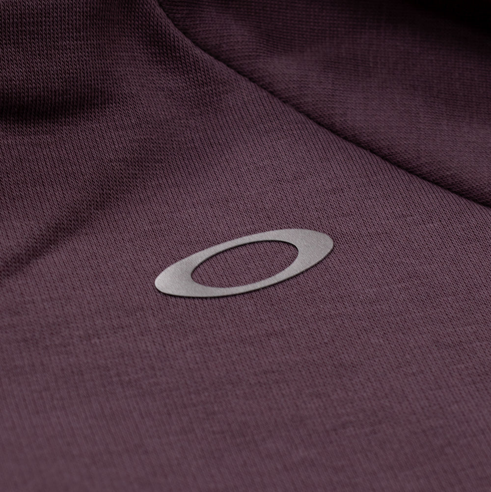 Extreme macro close-up of the right shoulder branding on the Oakley FGL Slick Fleece Hoodie, displaying the reflective silver heat-transfer Oakley Ellipse icon cleanly bonded onto the fine-gauge rouge fleece textile.