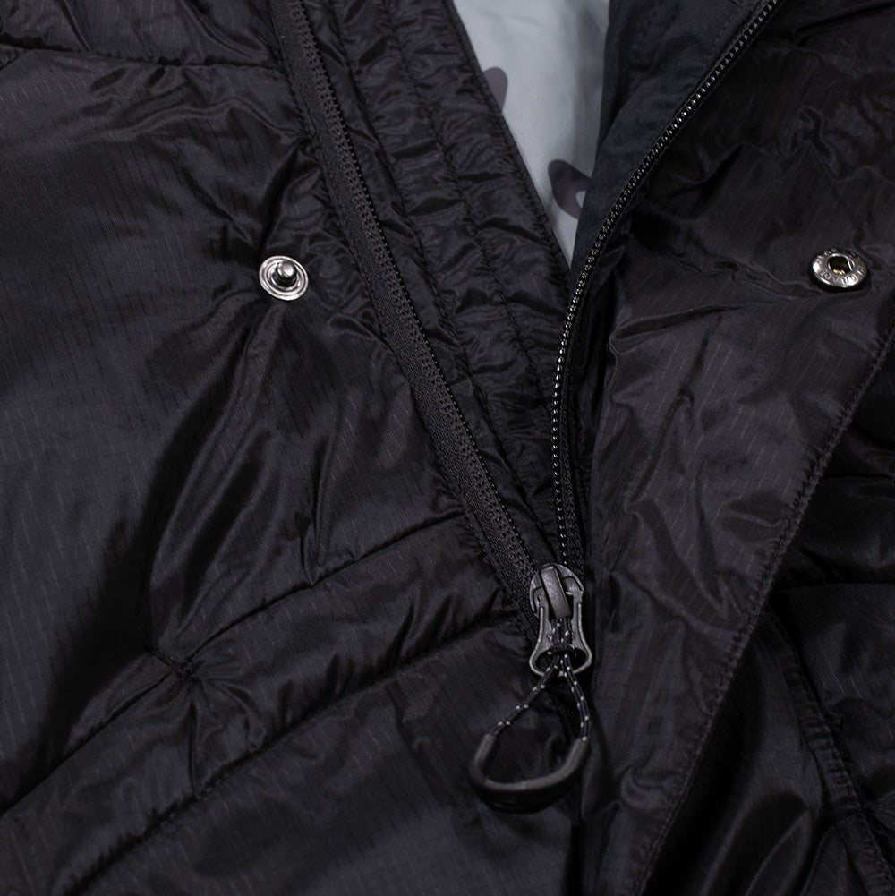 Macro studio view of the front closure on the Oakley FGL Stealth Ins Jacket 2.0, highlighting the dual-layer storm placket with embossed metal snap fasteners, heavy-duty black zipper track, and an ergonomic textured plastic cord puller.
