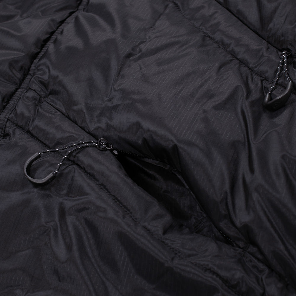 Close-up shot of the front utility pocket layout on the black Oakley FGL Stealth Ins Jacket 2.0, detailing the angled quilted down baffles and dual concealed zipper pockets equipped with reflective-flecked paracord loops and curved black finger pulls.