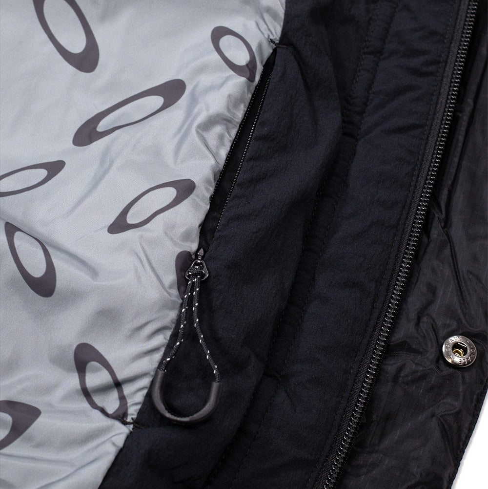 Macro studio close-up of the interior lining and placket on the Oakley FGL Stealth Ins Jacket 2.0, showcasing the smooth grey technical satin lining printed with an all-over repeating dark grey Oakley Ellipse logo pattern, an internal vertical zipper pocket, and an embossed inner metal snap.