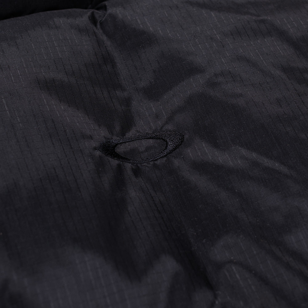 Extreme macro close-up of the front chest on the Oakley FGL Stealth Ins Jacket 2.0, detailing the tonal embroidered Oakley Ellipse logo cleanly integrated into the water-resistant, micro-textured black Schoeller ripstop textile.