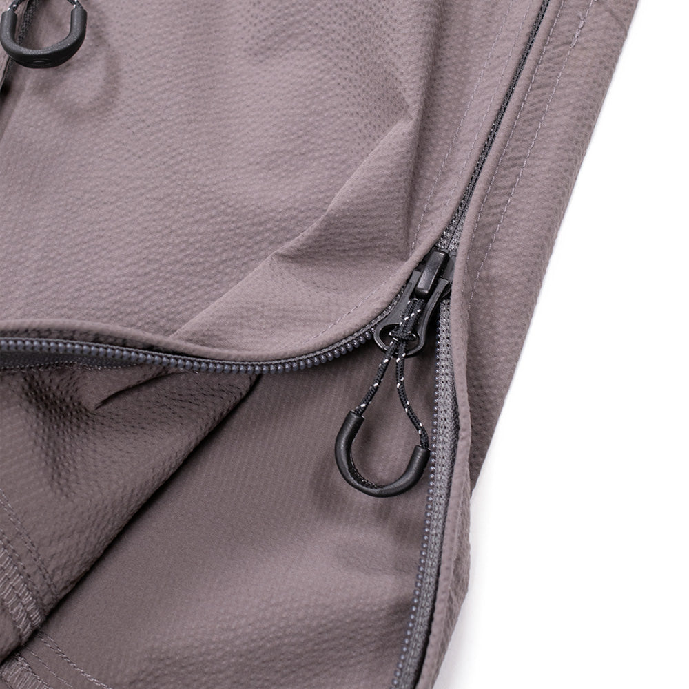 Macro studio perspective of the lower left side seam on the Oakley FGL Stroke Anorak in Gray Wash, highlighting the durable reverse-coil side entry zipper designed for easy pullover access, complete with an ergonomic pull tab and reinforced hem split construction.
