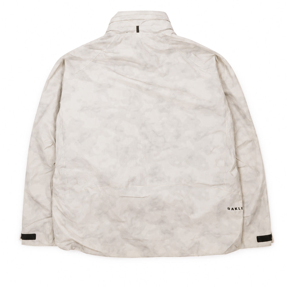 Back flat lay studio view of the Oakley Mthod Glow Shell Jacket in Reflective Camo Mist, displaying the cloud-like tonal grey camo print pattern, articulated shoulder seams, dropped tail hem, adjustable velcro cuff tabs, and clean black Oakley block lettering along the lower right back hem.