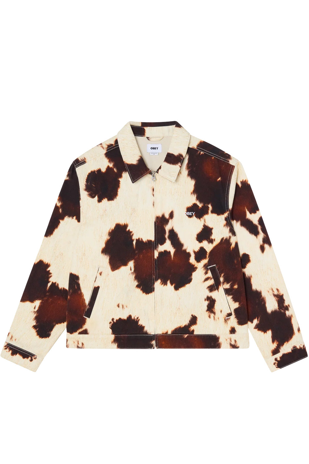 Front view of the Obey Workshop Jacket in Cow print, crafted from heavy 13.5oz 100% cotton denim with an all-over brown and cream cowhide pattern, pointed fold-down collar, silver metal full zip closure, slanted front welt pockets, and white embroidered Obey script branding on the left chest.