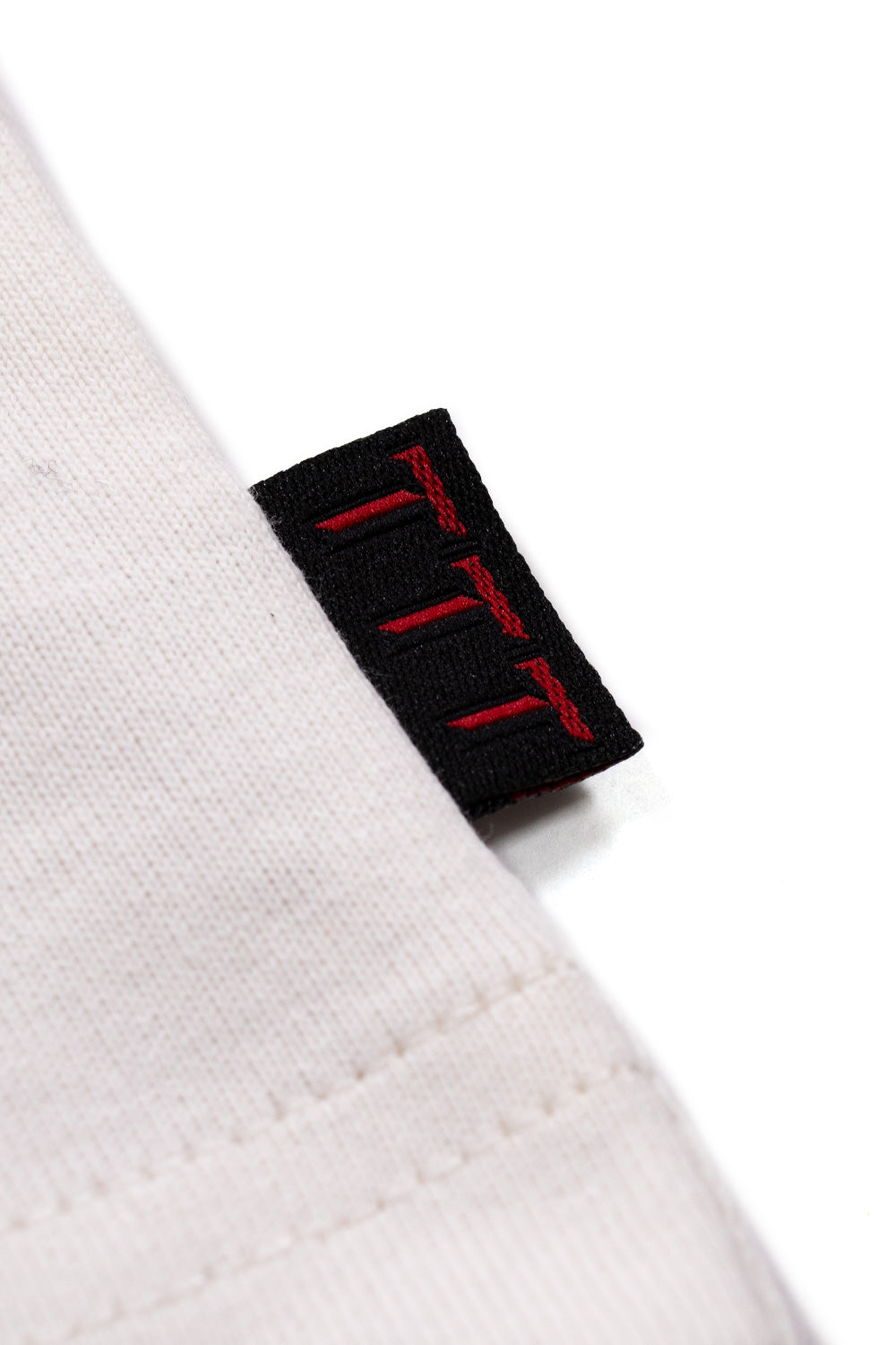 Detailed view of the woven TTT label on the left side seam of the The Trilogy Tapes Strung T-Shirt White, highlighting premium craftsmanship, durable heavyweight 100% cotton construction, oversized loose fit and authentic contemporary underground streetwear finish.