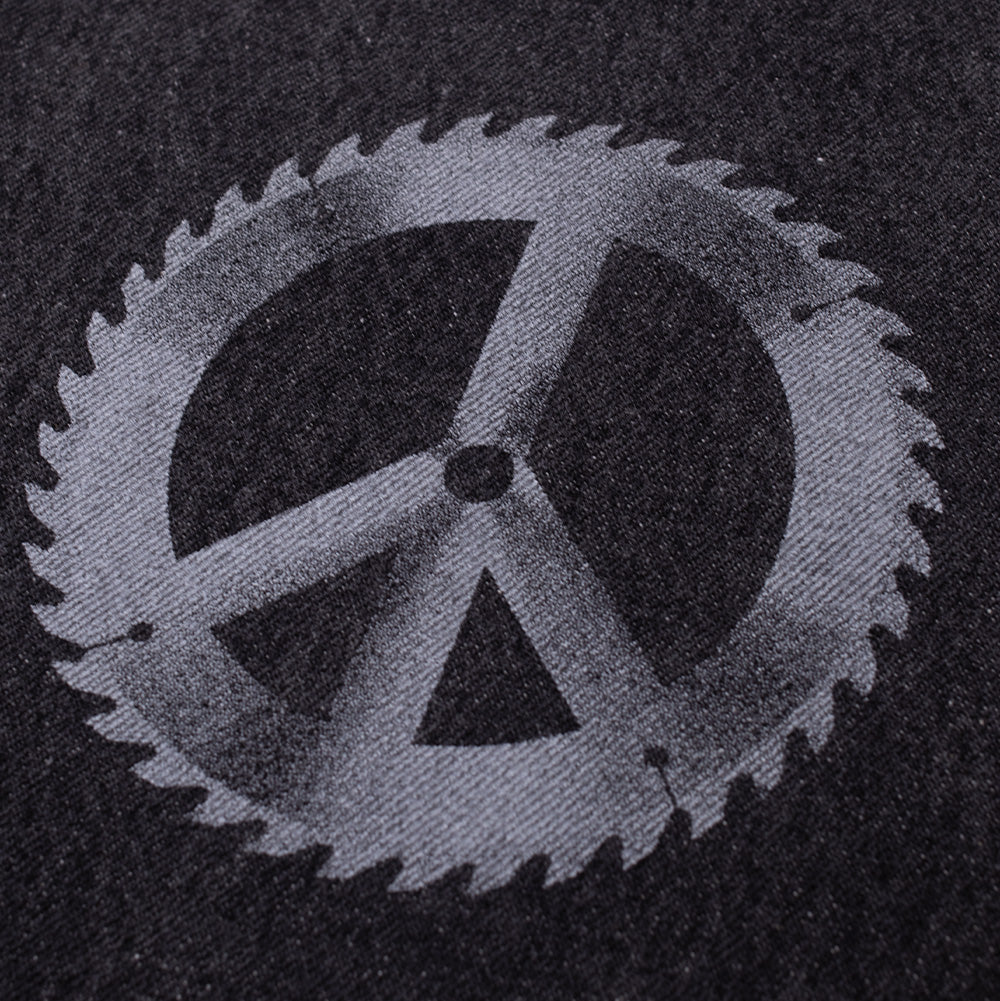 Detailed macro shot of the front leg graphic on the Token Alphabet Jeans, highlighting the distressed light grey screen-printed circular saw blade transformed into a classic peace sign on the textured black washed cotton denim.