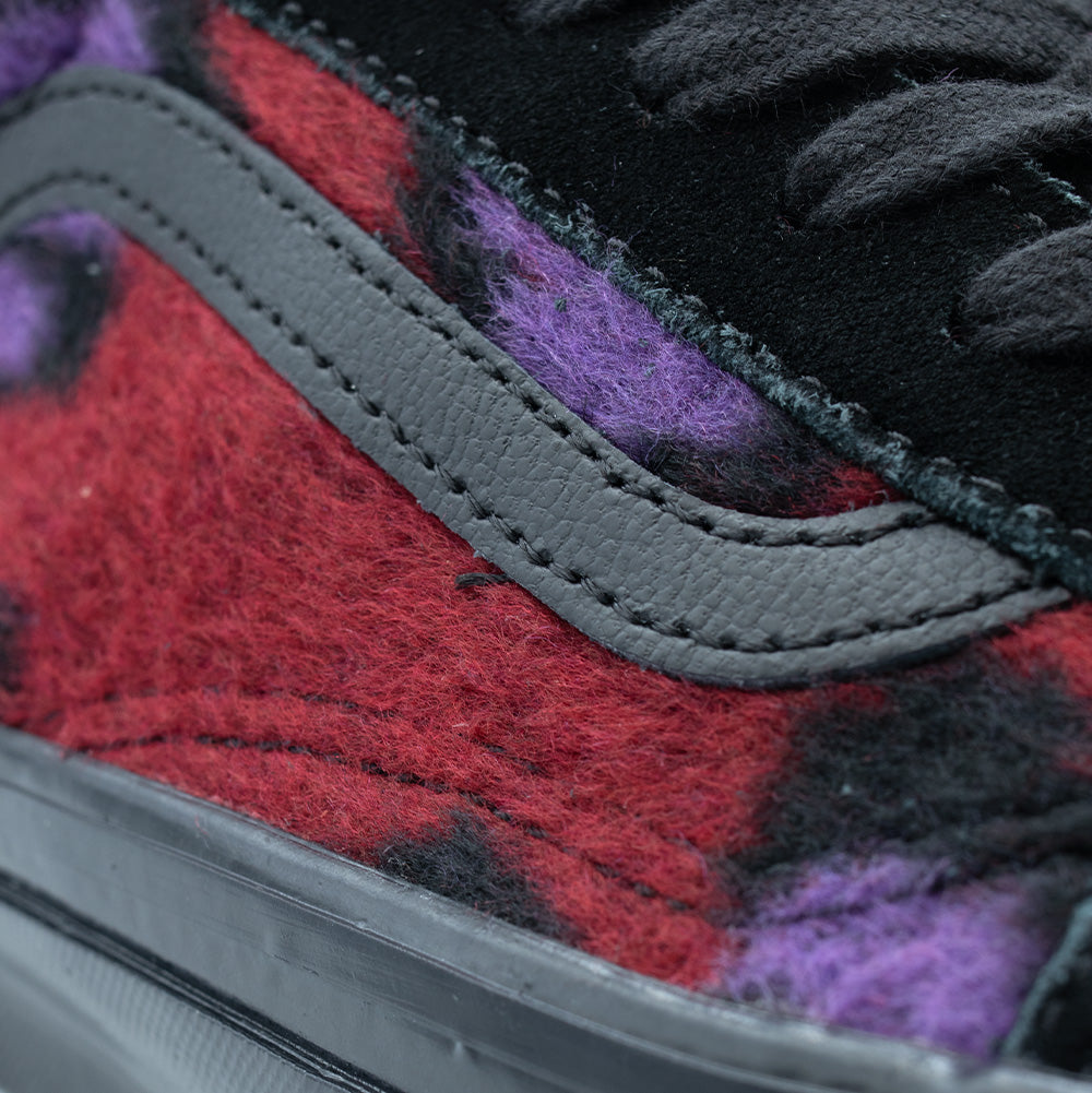 Extreme macro close-up of the quarter panel on the Vans LX Old Skool, detailing the dense, hairy pile of the red and purple leopard fleece, contrast double-stitched textured black leather Jazz Stripe, black suede eyestay, and the edge of the glossy black rubber foxing tape.