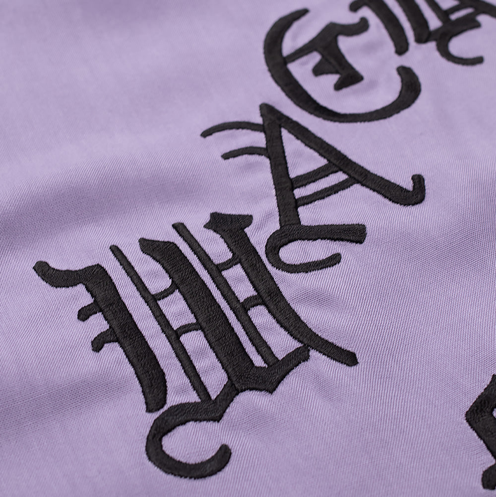 Extreme macro close-up of the back embroidery on the purple Wacko Maria 50's Shirt Type 3, detailing the tactile, high-density black thread embroidery outlining the gothic characters "WA" from the signature "WACKO MARIA" lettering against the soft lavender textile.