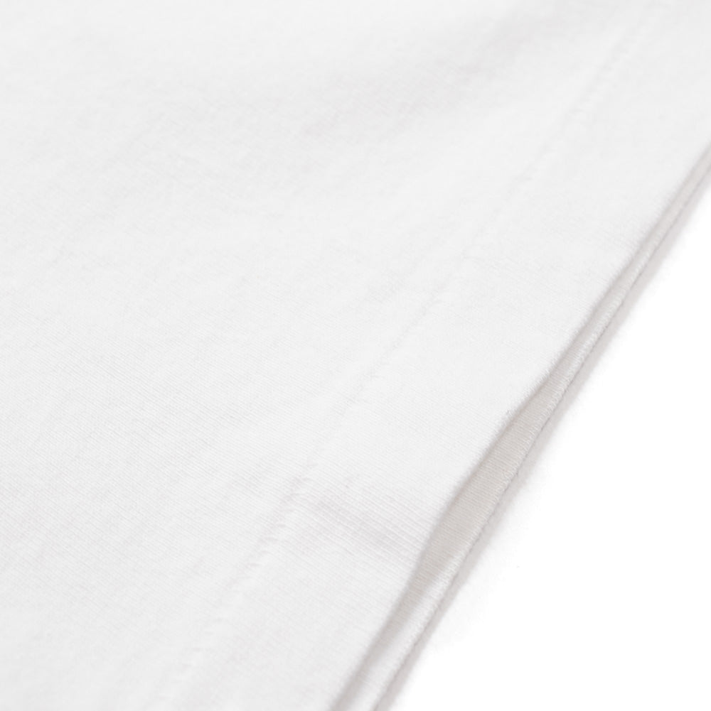 Extreme macro close-up of the sleeve cuff and hemline on the white Wacko Maria Washed Heavy Weight Crew Neck T-Shirt, highlighting the substantial, tightly woven knit texture of the washed cotton fabric finished with tonal parallel double-needle stitching.