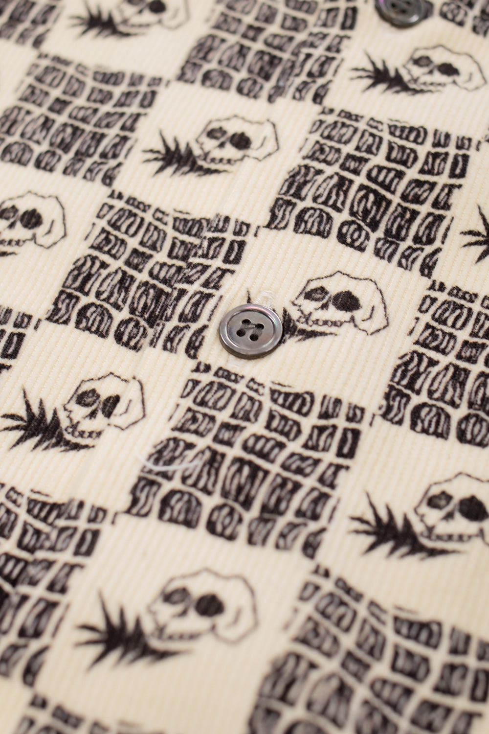 macro image of mother-of-pearl button on Wacko Maria 50s shirt Type-1, showcasing fine cotton corduroy texture, high-end Japanese craftsmanship and unique skull print design