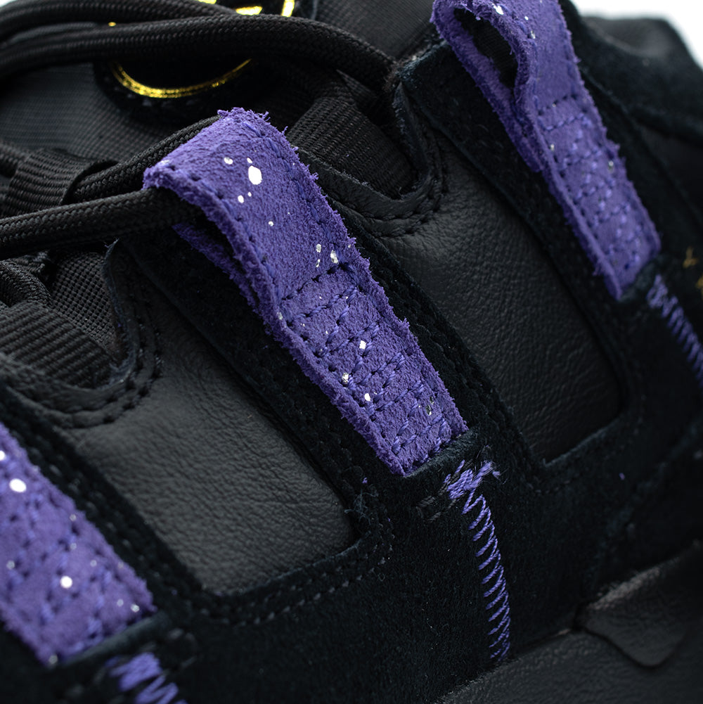 Detailed macro studio close-up of the lateral eyelet straps on the adidas Kader shoe, focusing on the rough hairy texture of the Collegiate Purple suede Three Stripes embedded with metallic silver glitter specks, set against durable black leather underlays and thick round black laces.