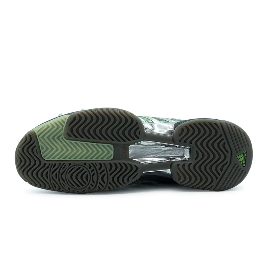 Full studio flat lay of the segmented adidas x Brain Dead Barricade V rubber outsole, featuring multi-directional herringbone traction treads in dark carbon and olive green, a high-shine chrome Torsion System midfoot plate, and a green embossed adidas badge on the heel.
