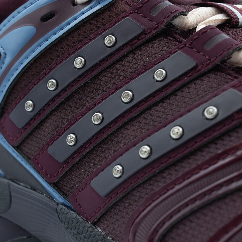 Macro close-up shot of the lateral Three Stripes on the Adidas X Hardies Adistar Control 5, detailing the dark maroon synthetic bands embedded with glistening silver crystal rhinestones atop the textured wine-red mesh base.