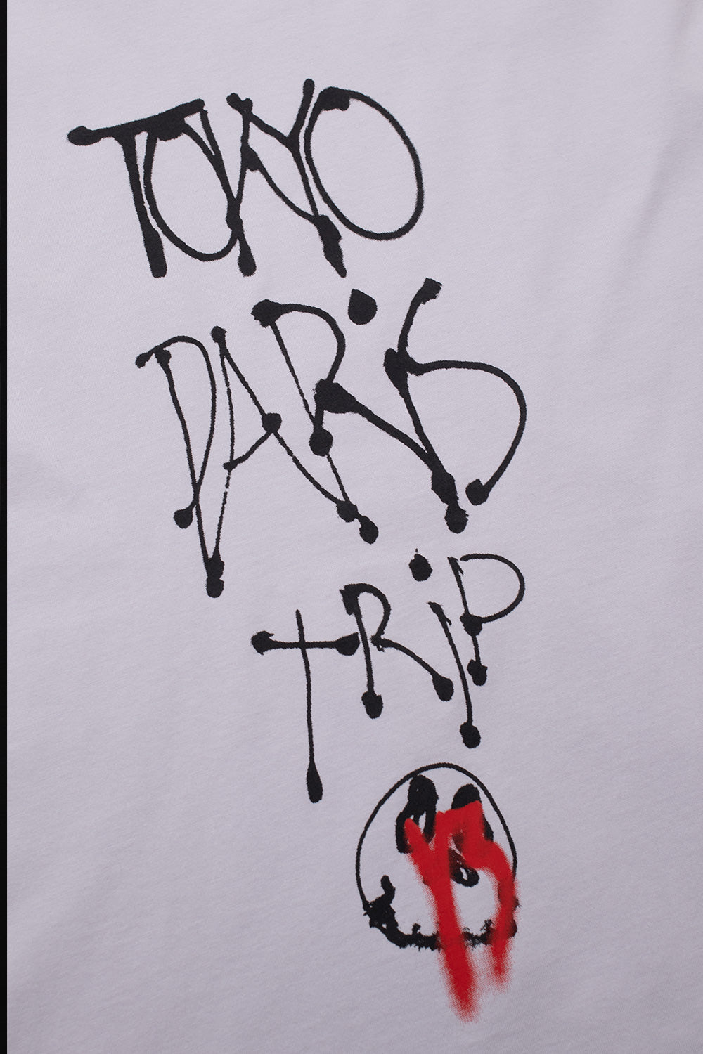 Close-up of the black dripped Tokyo Paris Trip spray paint lettering and sprayed red smiley face artwork on the chest of the Adidas Y-3 x Chito capsule collection tee.