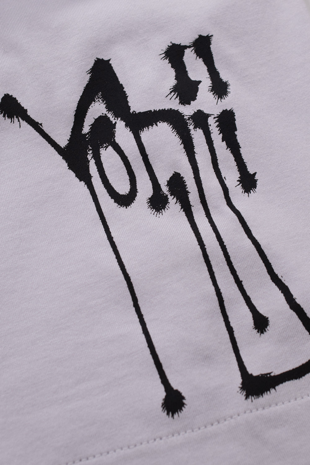 Detailed view of the black airbrushed dripped Yohji signature graffiti tag printed on the left sleeve hem of the Adidas Y-3 x Chito KX3816 T-shirt.