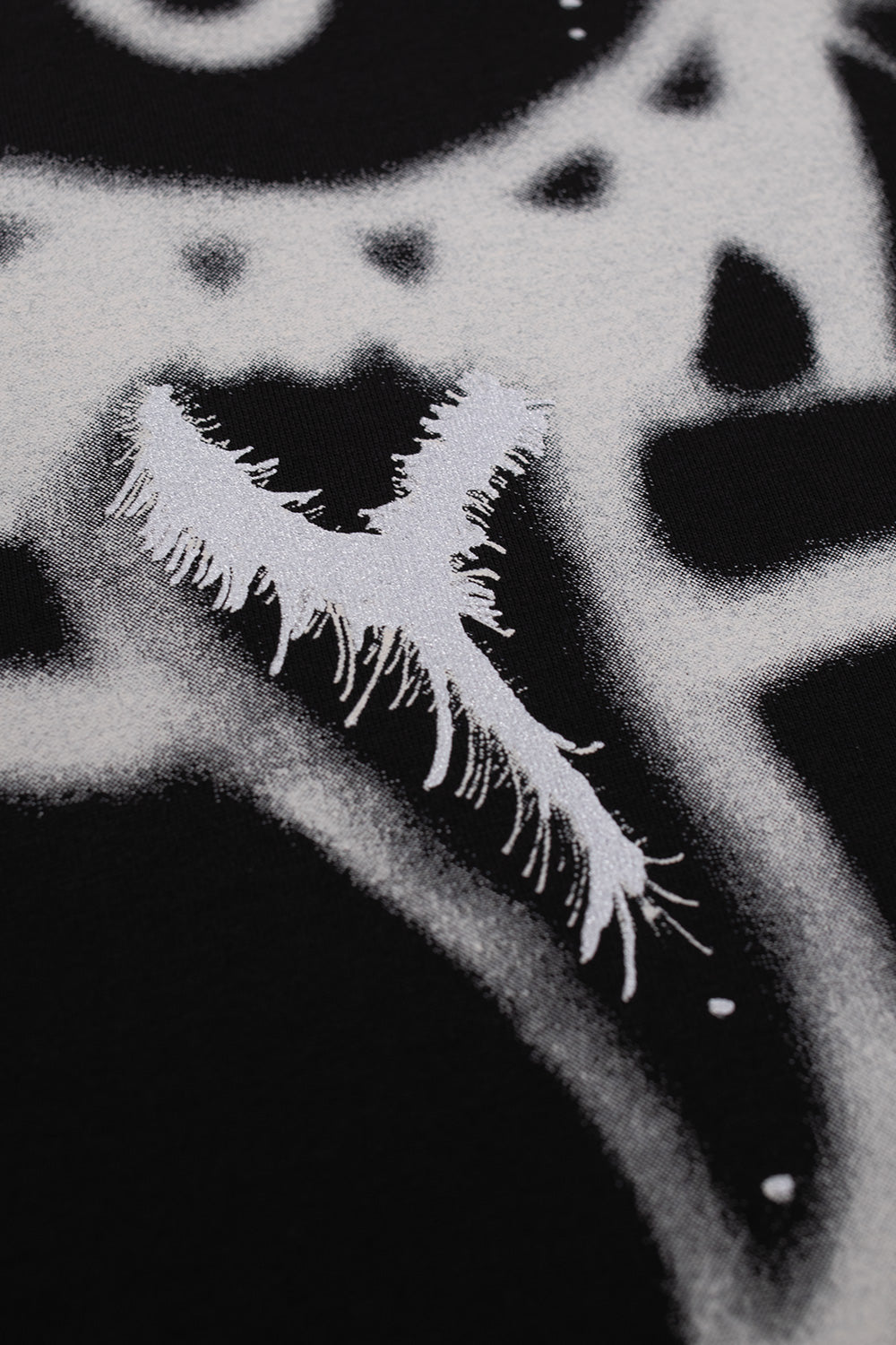 Macro detail shot of the lower jaw and tongue section of the white airbrushed creature graphic on the black Adidas Y-3 X Chito collaboration T-shirt, showcasing intricate sprayed half-tone mist and textured brush strokes.