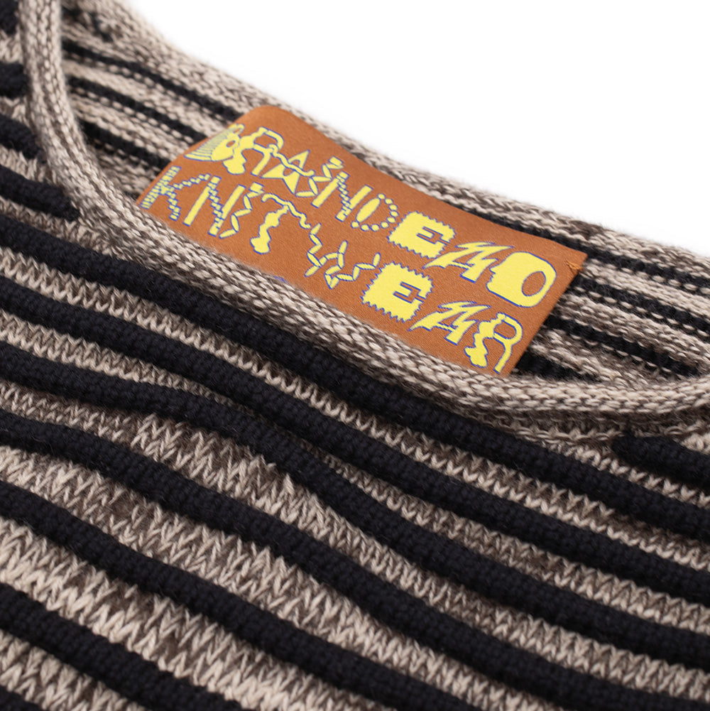Detailed macro studio close-up of the crewneck collar on the Brain Dead 3D Wave Cropped Sweater, highlighting the orange woven interior neck tag displaying yellow cartoon-style "BRAIN DEAD KNITWEAR" lettering, bordered by the ribbed knit neckline and horizontal raised black wave stripes traversing the textured ash marl knit base.