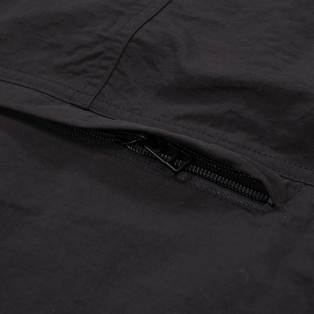 Macro perspective of the rear storage compartment on the black Brain Dead Dolman Sleeve Jacket, focusing on the horizontal concealed zipper track slightly opened beneath the protective fabric flap across the lower back panel.
