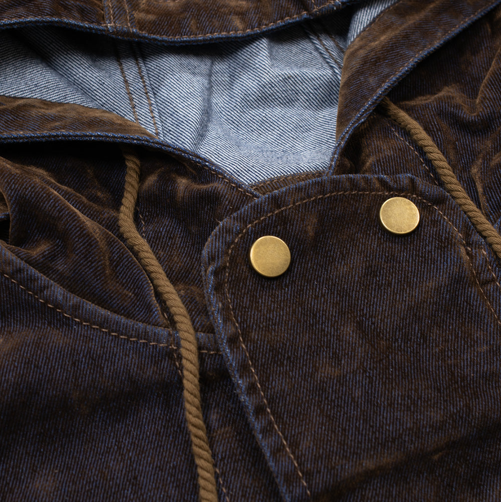 Detailed macro studio close-up of the hood and high-neck closure on the Brain Dead Fireman Jacket, highlighting the raw blue denim underside of the hood, braided brown drawstrings, and the overlapping storm flap secured with two circular antique brass snap buttons set into the tactile brown-flocked denim surface.