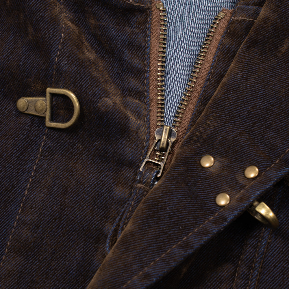 Close-up shot of the front closure mechanism on the Brain Dead Fireman Jacket, displaying the unlatched brass clasp, antique gold-tone metal two-way zipper teeth, triple brass reinforcement rivets on the storm flap, and the contrasting diagonal twill weave of the flocked brown denim fabric.