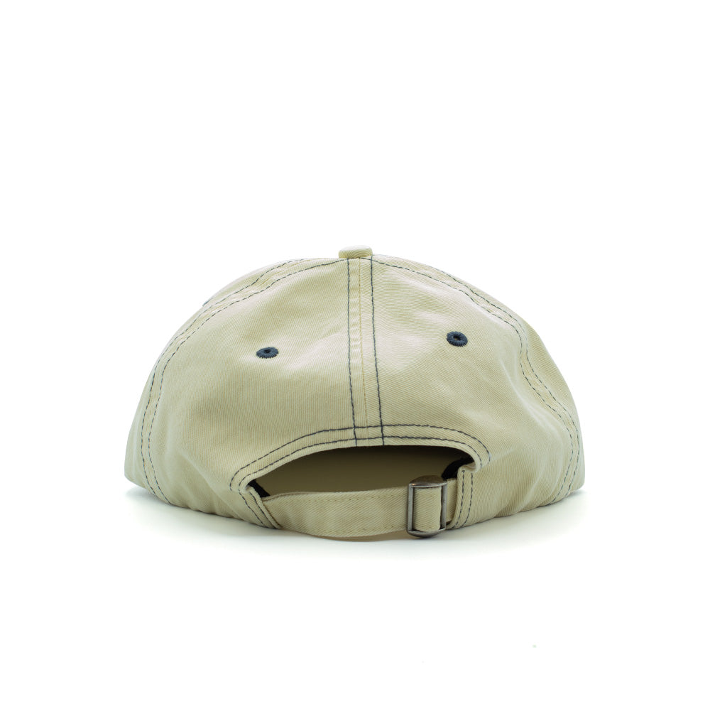 Rear studio perspective of the natural cream By Parra Lowercase Script Logo 6 Panel Hat, highlighting the matching self-fabric cotton strapback closure with an antique-brass metal slider buckle, embroidered navy eyelets, and clean contrast panel seam stitching.