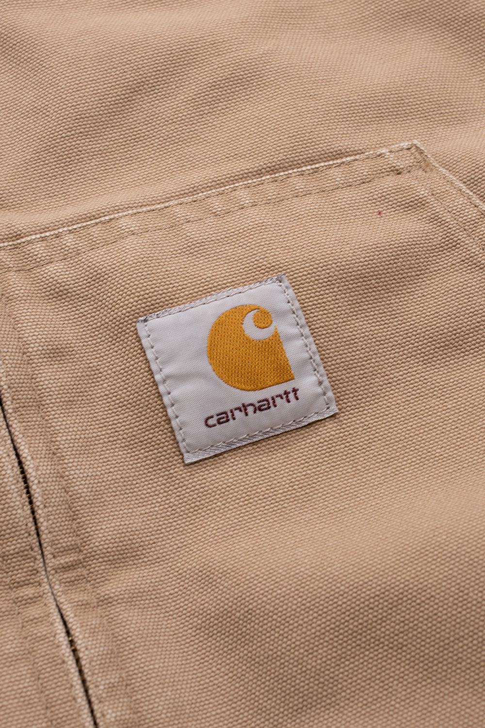 "Nahaufnahme des gewebten Carhartt-Logos auf der OG Active Jacket in Peanut Aged Canvas – hochwertiges Detail auf strapazierfähigem Canvas-Material"