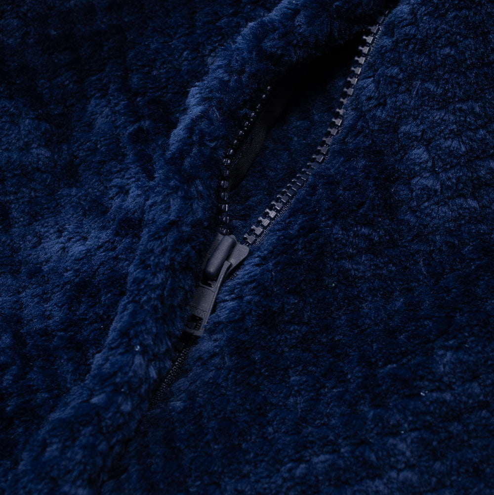 Close-up studio perspective of the secure pocket closure on the Dancer Fleece Half Zip, focusing on the hidden dark navy YKK coil zipper with branded slider embedded within the fluffy, high-pile fleece pile.